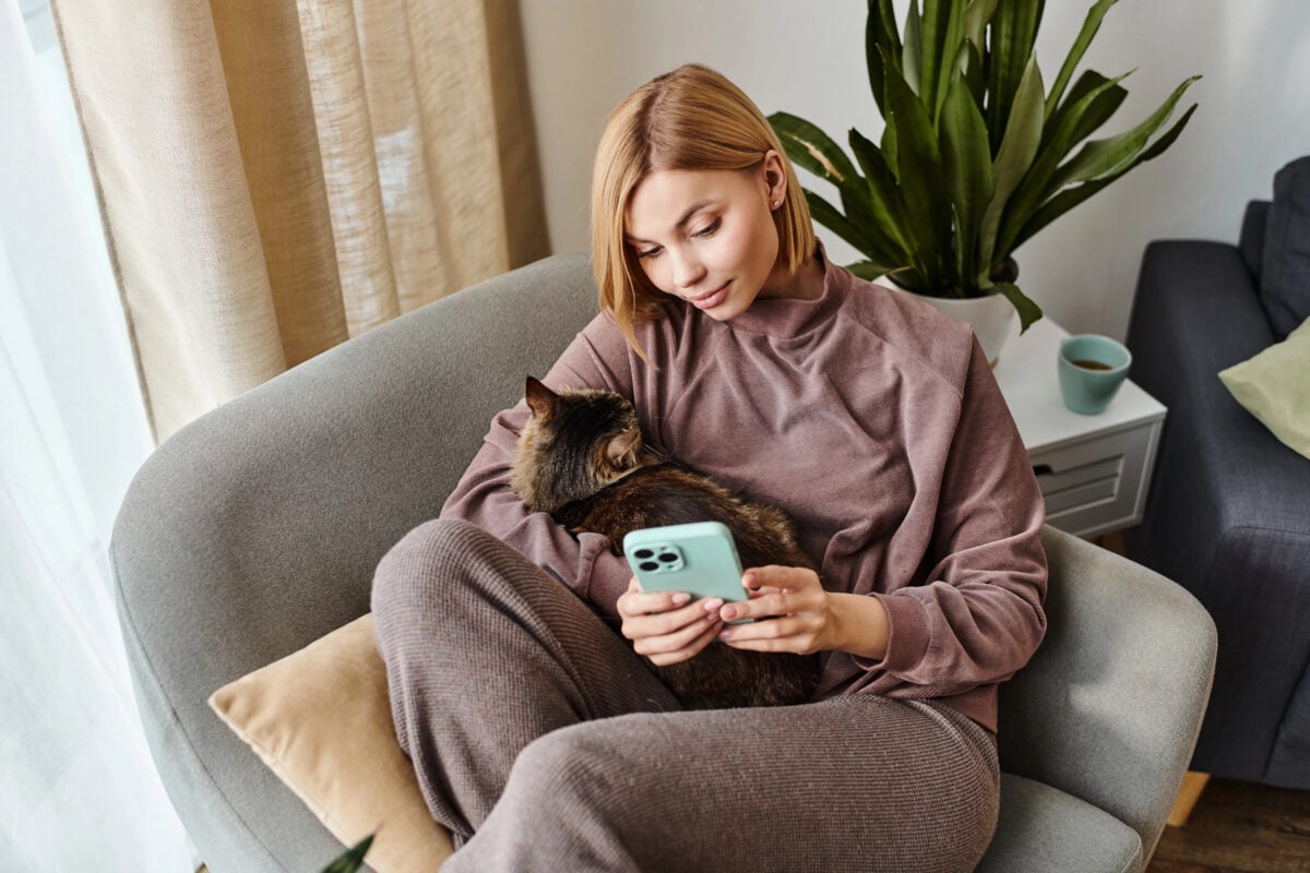 A woman with short hair relaxes in a chair, her cat peacefully resting on her lap as they enjoy a moment of calm.