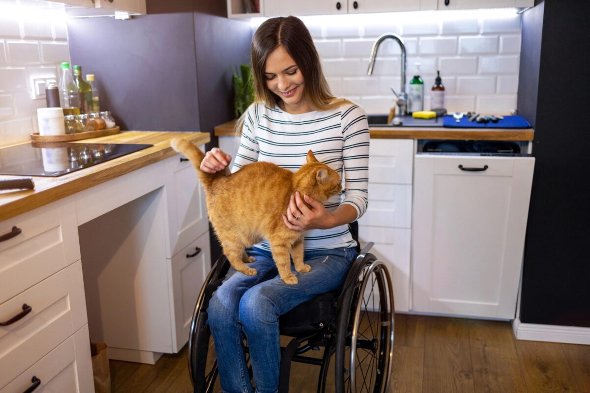 Disabled young woman in kitchen with cat on her lap